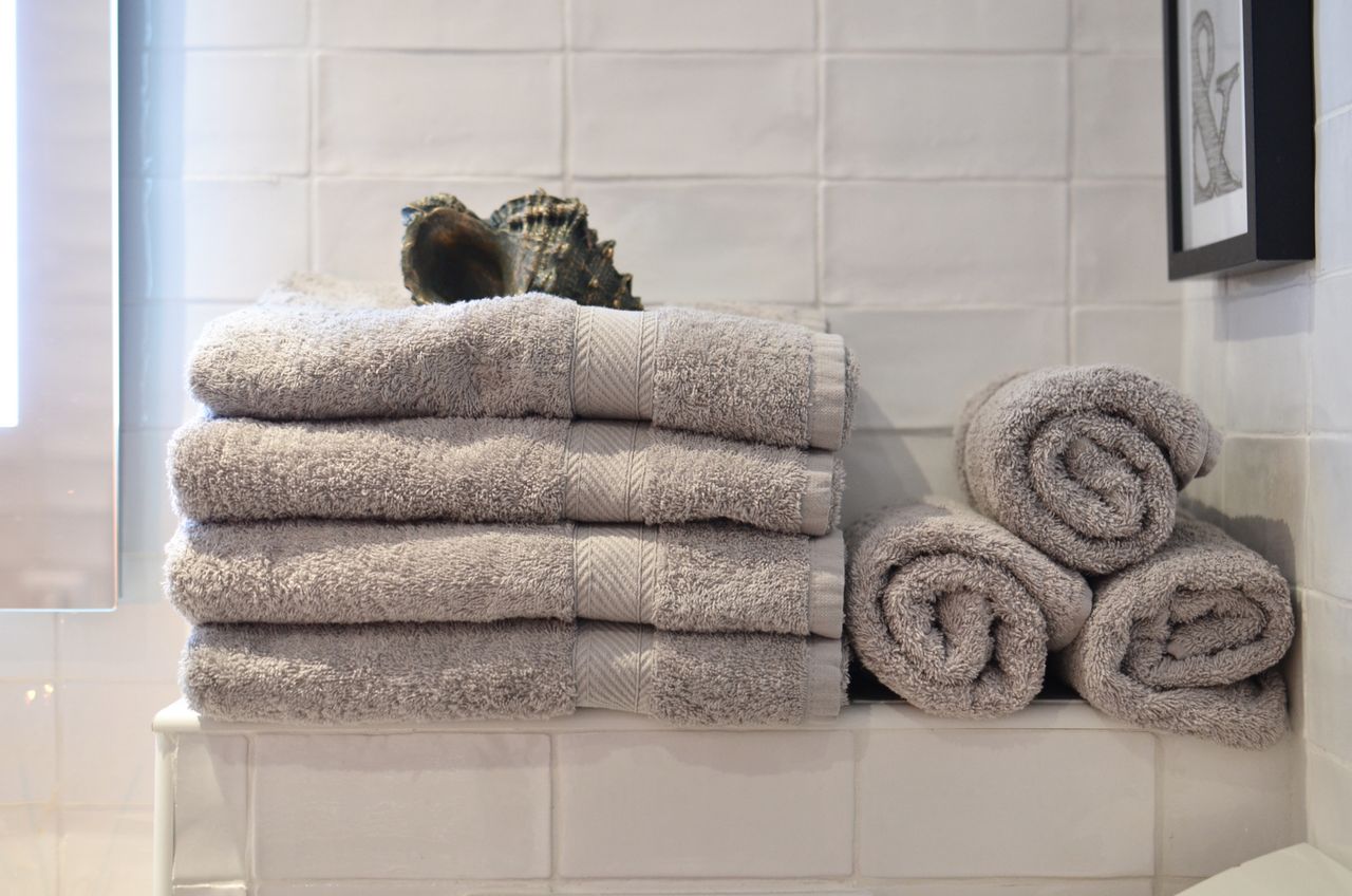 Big shell placed on heap of soft gray towels arranged on shelf near white tiled wall in modern bathroom